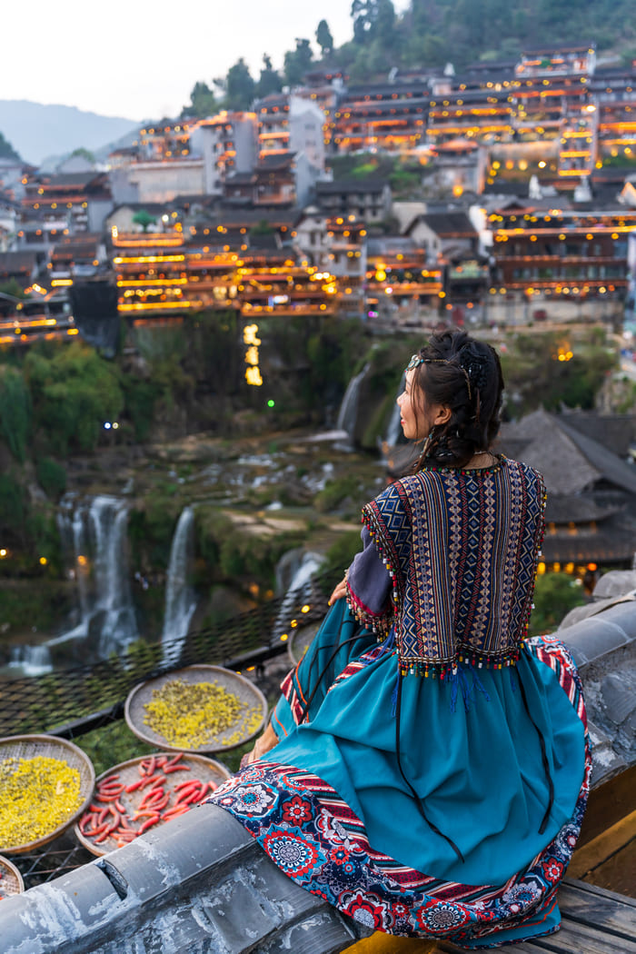 mujer China sentada con un vestido tipico, mirando las montañas en China y con bandejas de comida